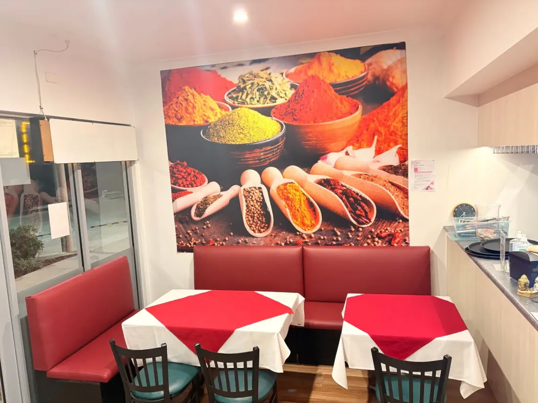 Inside Indique: red banquette seating and white-clothed tables beneath a large printed mural of Indian spices